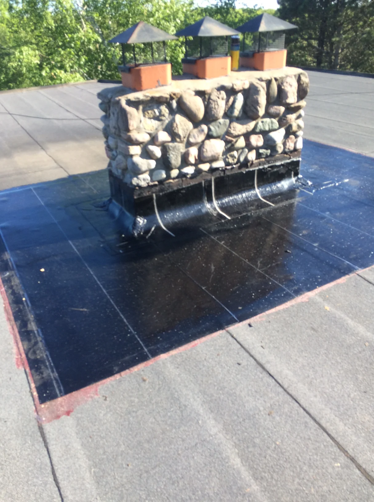 Stone chimney on a flat roof with new membrane flashing sealed around its base